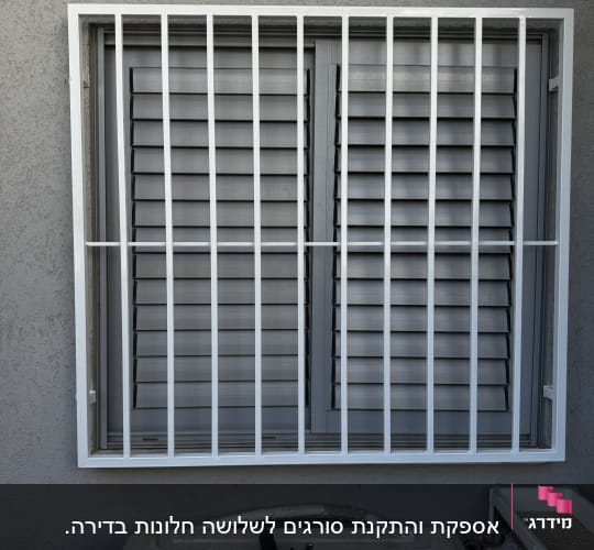 סורג מתכת על חלון עם תריסים אפורים